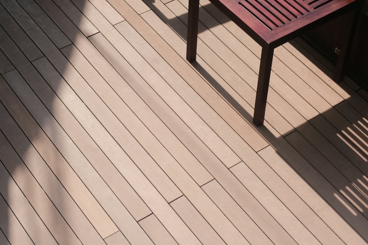 Sunlight casts shadows across a slatted wooden patio table.