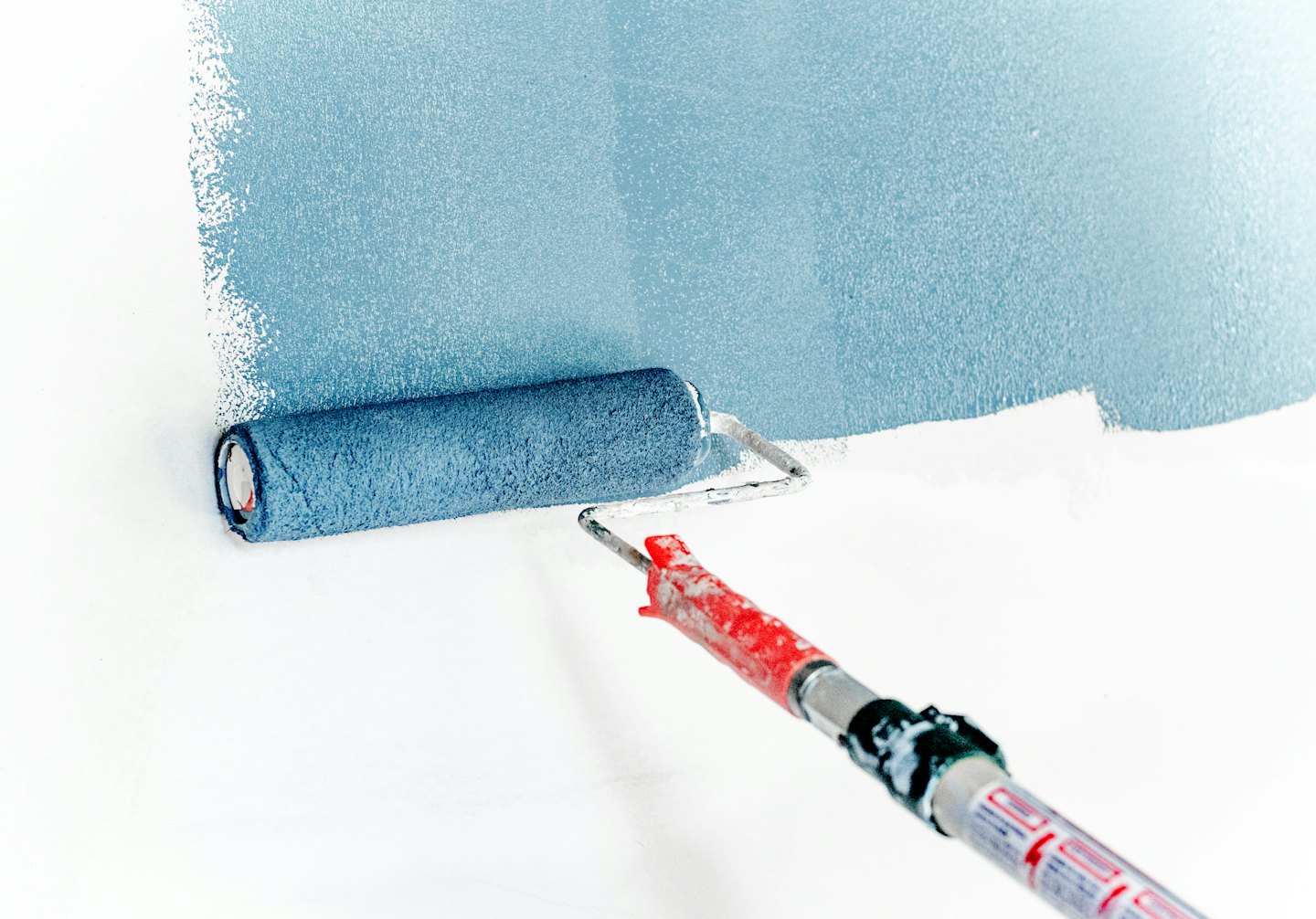 Paint roller applying light blue paint to a white wall.