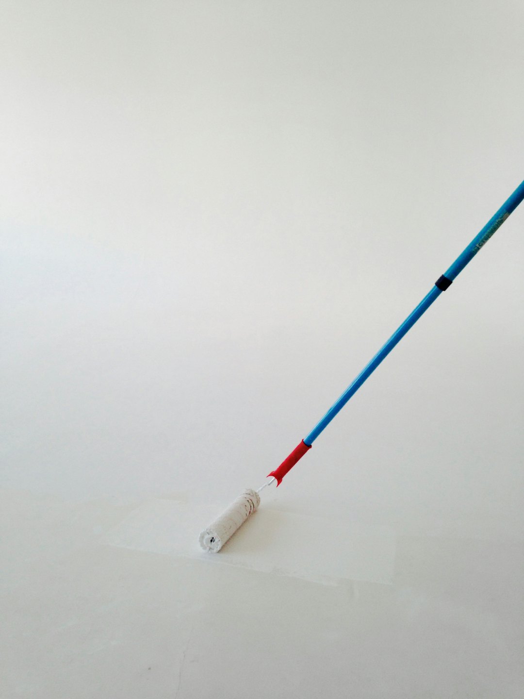 Painting a wall with a blue and red handled roller.